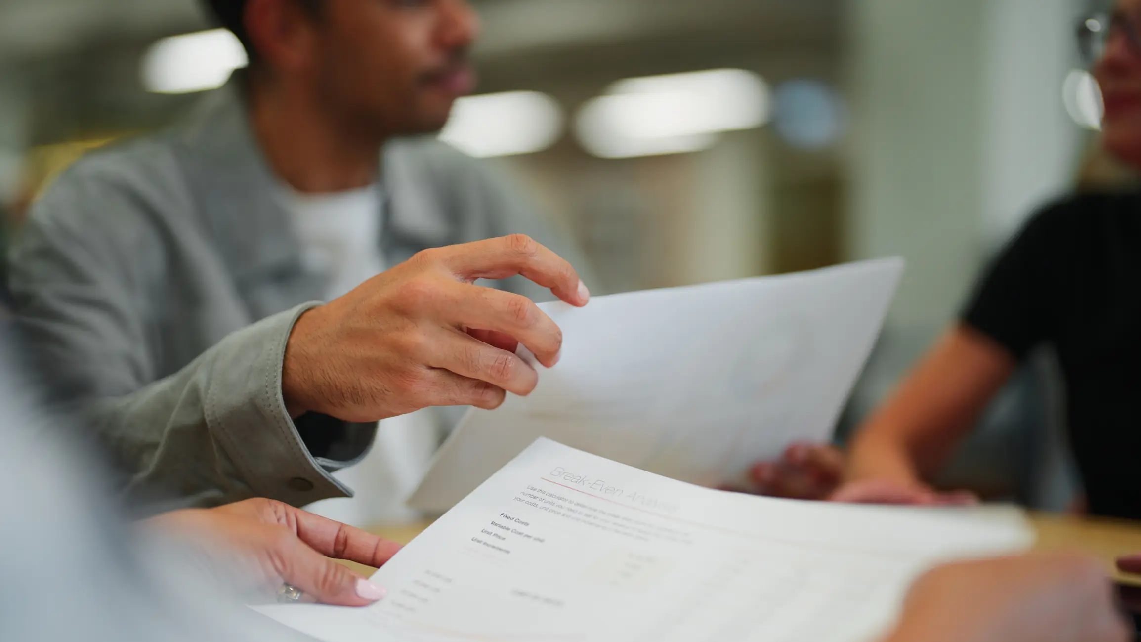 Hands exchanging business documents in a meeting.